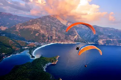 Aerial view of paragliders flying above Ölüdeniz Beach and its curved blue lagoon, surrounded by mountains near Fethiye, Turkey.