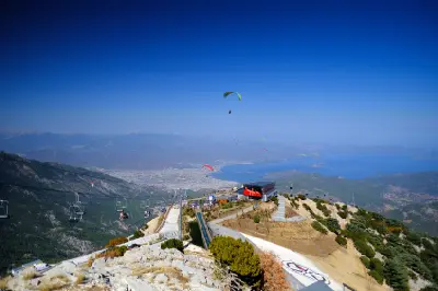 Paragliders flying from Babadağ summit above the cable car station, with Fethiye and the Mediterranean coast in the distance.