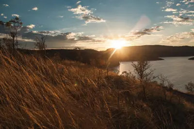 Setting sun casts golden light across dry grasses and rugged hills overlooking the waters of Lake Argyle.