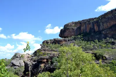 Tall, vertically weathered sandstone cliffs above rocky terraces and green woodland at Burrungkuy (Nourlangie) in Kakadu National Park, Australia.