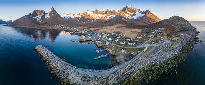 Aerial view of Mefjordvær village on Senja with harbour, breakwater, blue water, and jagged mountains in northern Norway