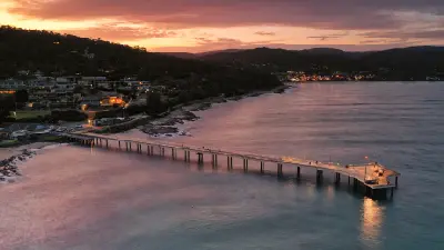 Aerial twilight view of Lorne Pier extending into the bay, with town lights glowing beneath the forested hills of Lorne, Victoria.