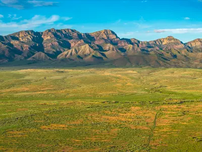 Close aerial view of the Elder Range's layered rocky cliffs above green and red plains near Moralana Scenic Drive, Flinders Ranges, South Australia.