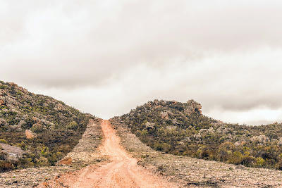 Remote gravel road between Eselbank and Wupperthal winding through rocky fynbos-covered hills in the northern Cederberg Mountains.