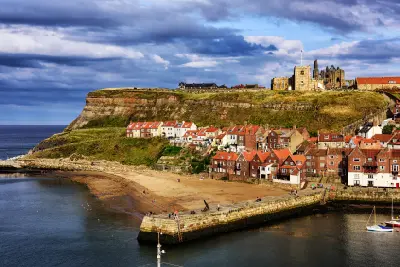 Wide view of Whitby harbour and beach with red-roofed houses below Whitby Abbey on the East Cliff, North Yorkshire, England.