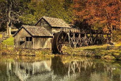 Historic wooden Mabry Mill with waterwheel and autumn foliage reflected in a pond along the Blue Ridge Parkway in Virginia.