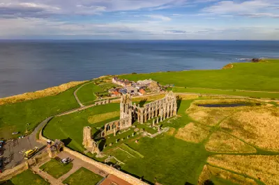 Aerial photograph of Whitby Abbey's medieval Gothic ruins on a green coastal headland overlooking the North Sea in North Yorkshire, England.