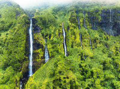 Multiple slender waterfalls descending mossy green cliffs at Poço da Ribeira do Ferreiro on Flores Island in the Azores.