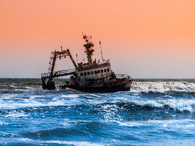 Close view of the Zeila shipwreck off Namibia’s Skeleton Coast with waves breaking around the rusting vessel at sunset.