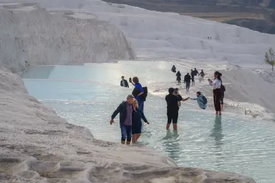 Visitors walking barefoot through shallow thermal pools among the white travertine terraces of Pamukkale, Turkey.