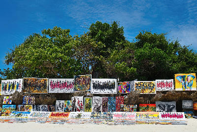 Vibrant African paintings and handmade artwork displayed at an open-air beach market on Kendwa Beach, Zanzibar, Tanzania.