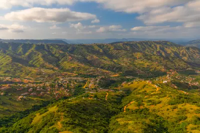 Elevated view of the Valley of a Thousand Hills showing green hillsides, winding roads, scattered settlements and layered valleys beneath a partly cloudy sky in KwaZulu-Natal.