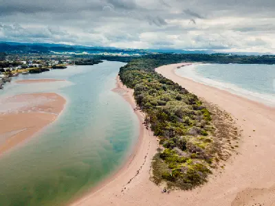 Aerial view of the Minnamurra River estuary with sandbars, coastal vegetation and beach beneath dramatic grey clouds.