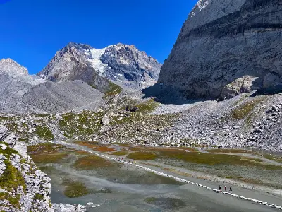People crossing stepping stones at Lac des Vaches with alpine peaks and glacier in the background in Vanoise National Park