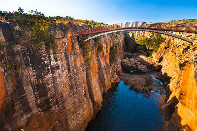Bridge crossing the sandstone gorge at Bourke’s Luck Potholes in Mpumalanga, South Africa, with steep rock walls, sculpted canyon formations and dark pools of water below.