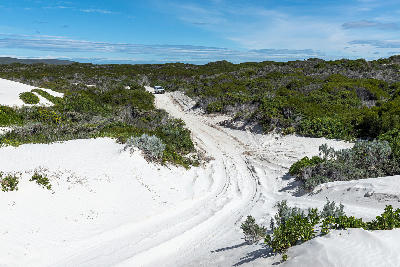 4x4 vehicle driving through coastal sand dunes and low fynbos vegetation at Struisbaai Plaat near Cape Agulhas, South Africa.
