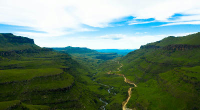 Aerial view of the Sani Pass valley with a winding mountain road, river and steep green escarpment slopes in the Drakensberg between South Africa and Lesotho.
