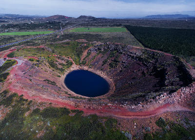 Drone view of Kerið crater in South Iceland with a circular dark blue lake and red volcanic rim.