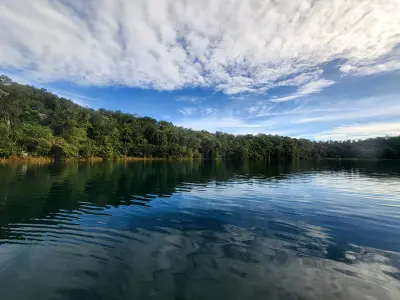 Lake Eacham with cloud reflections on dark blue water and a rainforest-covered shoreline in Queensland, Australia.