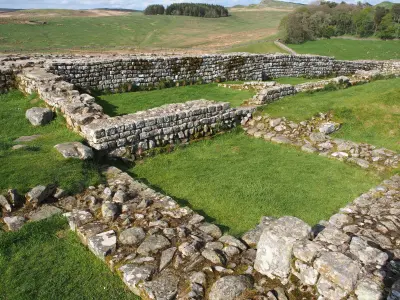 Rectangular stone foundations and grassy courtyards at Housesteads Roman Fort, with rolling Northumberland hills in the background.