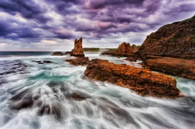 Waves surge through the rugged rock formations of Cathedral Rocks beneath dramatic purple storm clouds near Kiama.