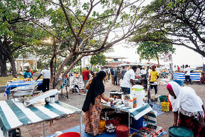 Local vendors setting up food stalls beneath shady trees at Forodhani Gardens in Stone Town, Zanzibar, before the evening market opens.