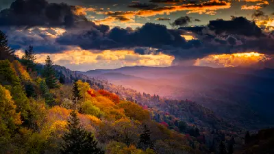 Golden autumn forest and layered mountain valleys beneath dramatic storm clouds at Oconaluftee Overlook in Great Smoky Mountains National Park.