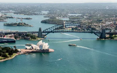 Aerial view of Sydney Harbour with the Sydney Opera House, Harbour Bridge and boats crossing the water.