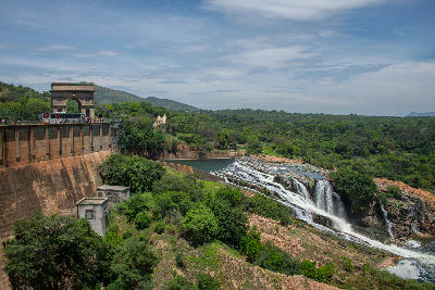 Hartbeespoort Dam wall and archway above the Crocodile River spillway, with water flowing over rocky cascades surrounded by dense green vegetation and mountain slopes.