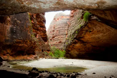 Towering striped sandstone walls enclose the sandy floor and small waterhole of Cathedral Gorge in the Bungle Bungle Range.