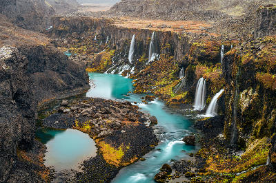 Sigöldugljúfur Canyon in the Iceland Highlands during autumn, showing numerous narrow waterfalls flowing into bright blue pools between dark volcanic cliffs.