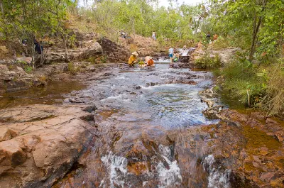 Visitors sitting beside shallow flowing rock pools and small cascades at Buley Rockhole in Litchfield National Park, Northern Territory, Australia.