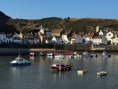 Small colourful fishing boats moored in Staithes Harbour, with traditional stone and whitewashed cottages lining the waterfront in North Yorkshire, England.