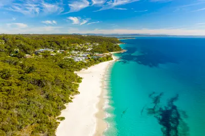 Brilliant turquoise water meets the white sands of Hyams Beach, with the small coastal village surrounded by dense bushland along Jervis Bay.