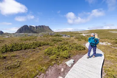 Hiker on an alpine boardwalk with Cradle Mountain rising in the background in Tasmania, Australia.