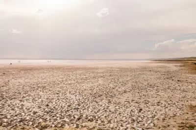 Wide view across the dry, textured salt crust of Lake Tuz with shallow water and distant visitors beneath a hazy sky in Turkey.