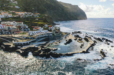 Aerial view of the natural lava pools in Porto Moniz, Madeira, with black volcanic rock formations and Atlantic Ocean waves surrounding the pools.