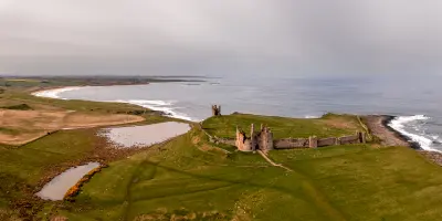Aerial panorama of Dunstanburgh Castle ruins, Embleton Bay, green coastal headlands and the North Sea in Northumberland, England.