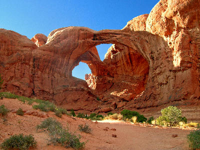 Double Arch viewed from below, showing two connected sandstone arches against a clear blue sky in Arches National Park, Utah.