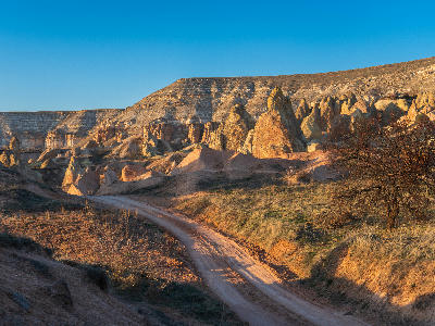 Dirt hiking trail winding through the colourful volcanic rock formations of Red Valley in Cappadocia, Turkey, illuminated by warm golden-hour light.