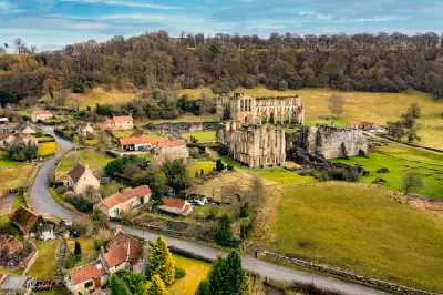 Elevated aerial view of Rievaulx Abbey showing its ruined Gothic church, surrounding stone buildings and wooded valley in the North York Moors.