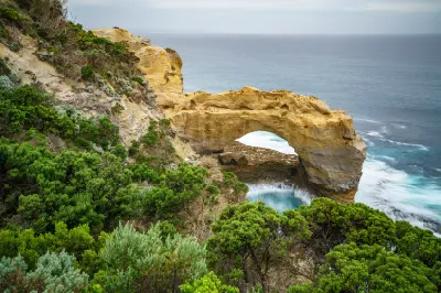 Limestone formation of The Arch framed by dense coastal vegetation above the Southern Ocean, Victoria.