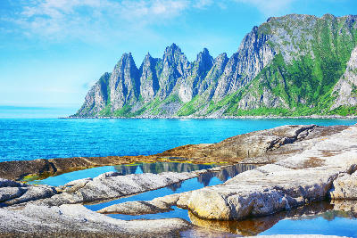 Jagged Okshornan peaks above Ersfjord with foreground tidal rock pools on Senja Island