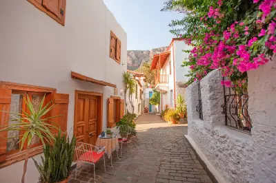 Narrow cobbled lane in Kaş lined with whitewashed houses, wooden shutters, potted plants and bright pink bougainvillea.