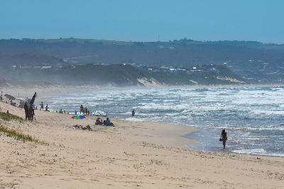 Visitors relaxing on the sandy shoreline of Diaz Beach near Mossel Bay, with ocean surf, coastal dunes and beachfront communities along the Garden Route.