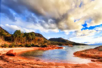 Pink granite beach and calm sheltered water at Honeymoon Bay glowing in warm evening light beneath dramatic clouds, Freycinet National Park, Tasmania.