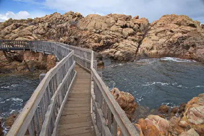 Wooden boardwalk crossing an ocean channel between rugged granite formations at Canal Rocks near Yallingup, Western Australia.
