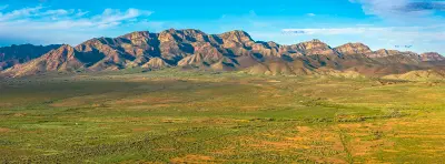 Panoramic view of the Elder Range's rugged layered cliffs above green plains near Moralana Scenic Drive in the Flinders Ranges, South Australia.