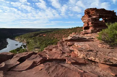 Nature’s Window stands above a red sandstone ledge with the Murchison River and vegetated gorge stretching into the distance.
