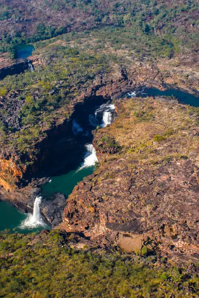 Aerial view of Mitchell Falls cascading through multiple sandstone tiers and pools, with Big Mertens Falls visible upstream in the distance.